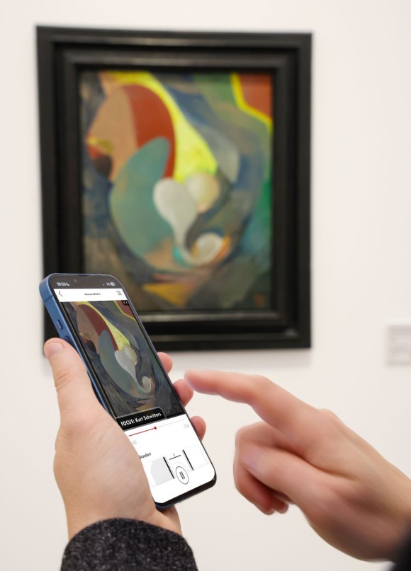 Ein Besucher scrollt durch die Sammlungsapp vor einem Kunstwerk von Kurt Schwitters.